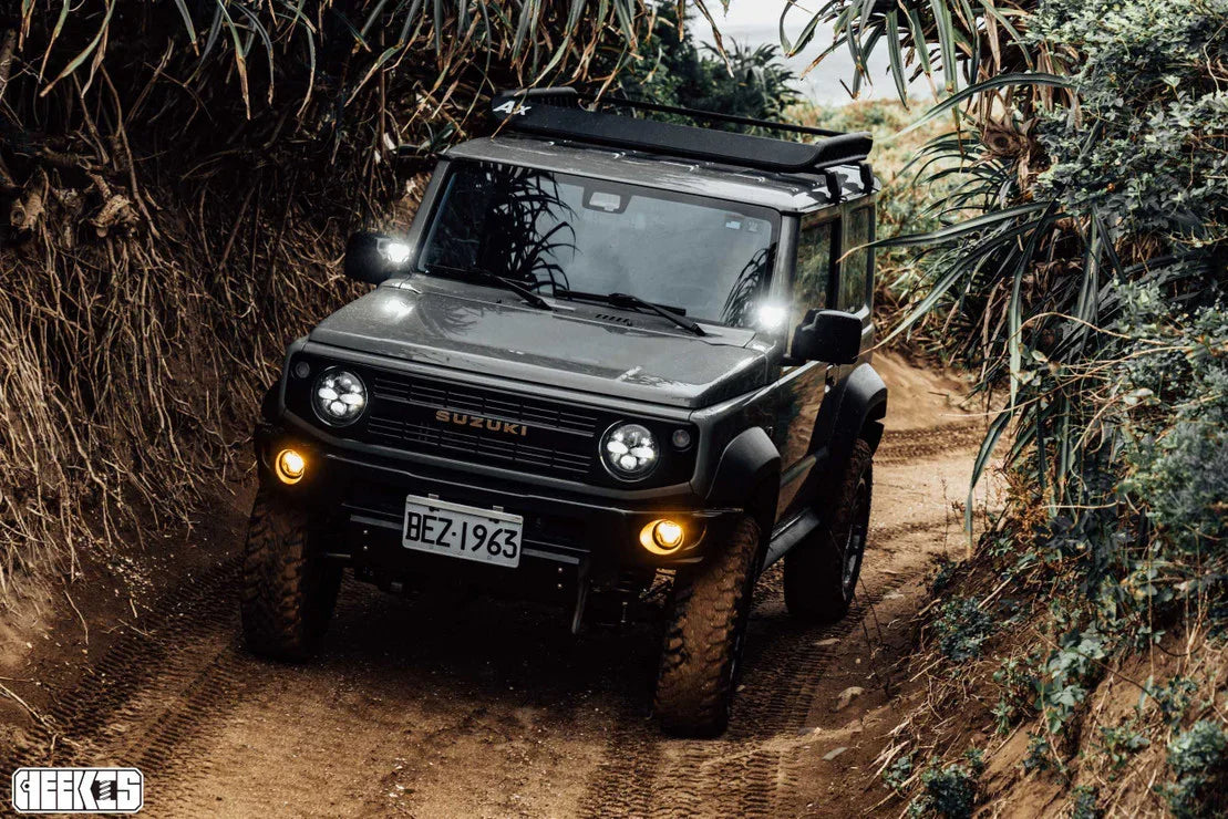 Suzuki 4x4 off-road vehicle driving on a rugged dirt trail with dense foliage