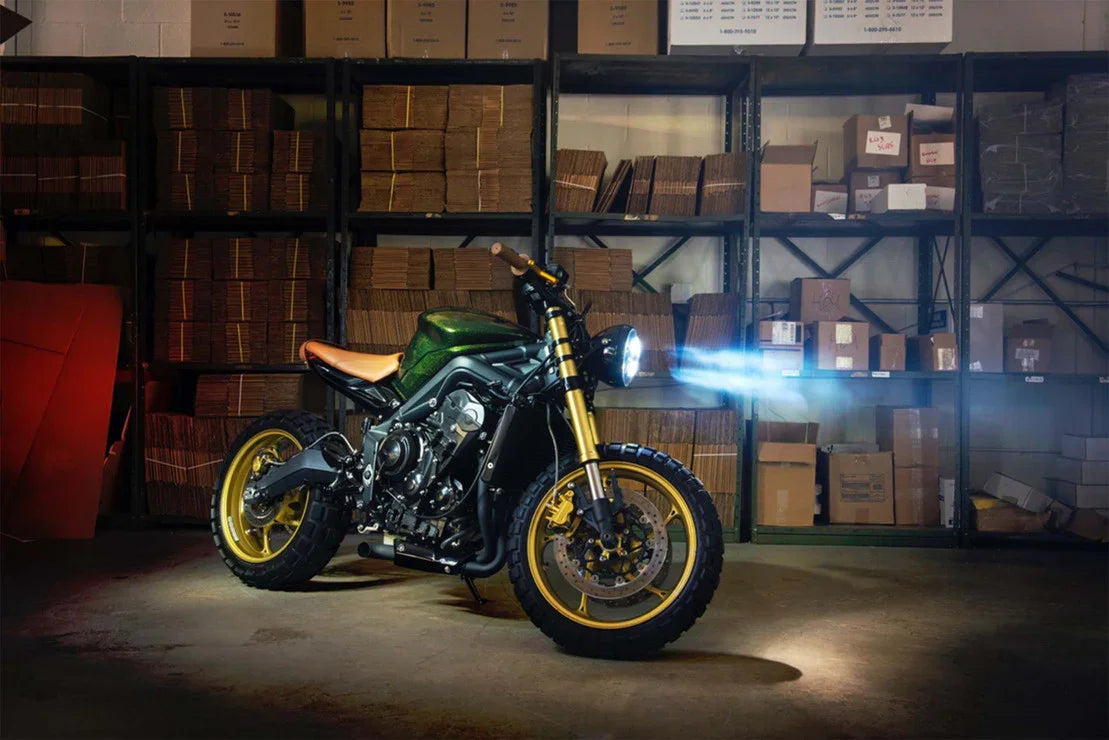 Custom adventure motorcycle with gold rims and illuminated headlight in warehouse setting