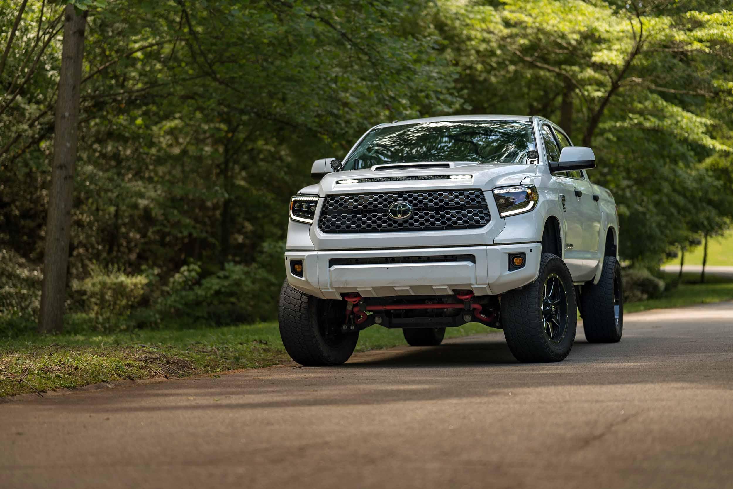 White Toyota Tundra with XB LED headlights on upgraded wheels parked on forest road