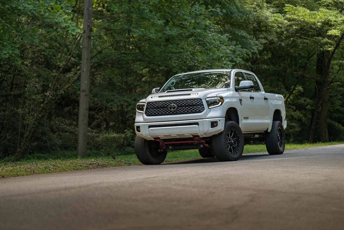 White Toyota Tundra truck with upgraded LED headlights parked on a forest road