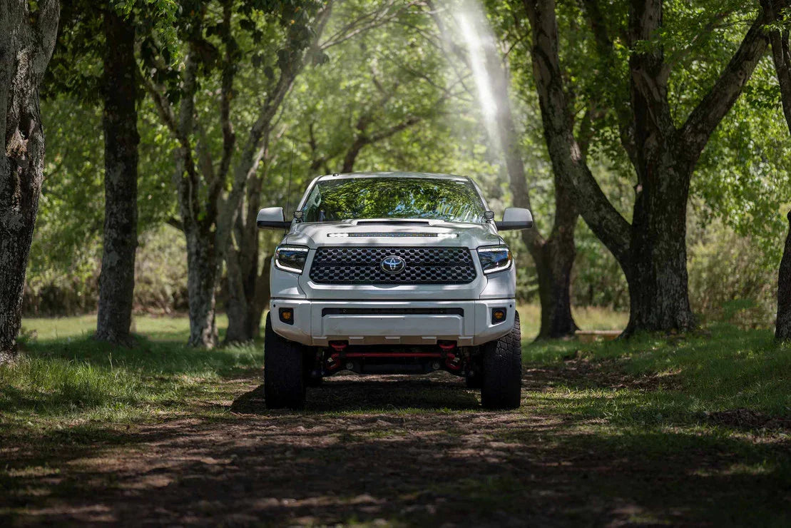 White Toyota Tundra with LED headlights parked on a forest trail under sunlight