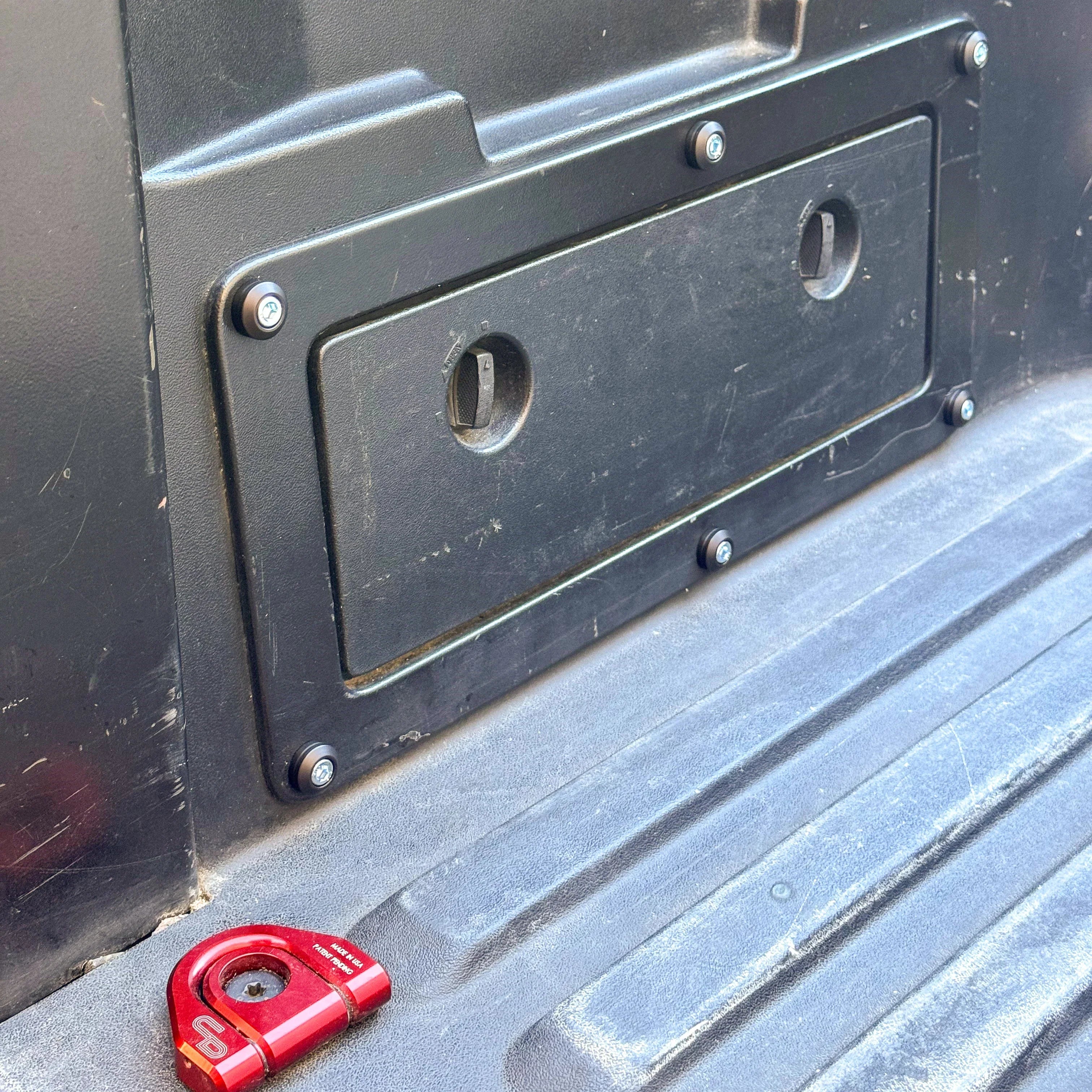 Close-up of Toyota Tacoma truck bed storage panel with dress-up hardware and a red tie down point.