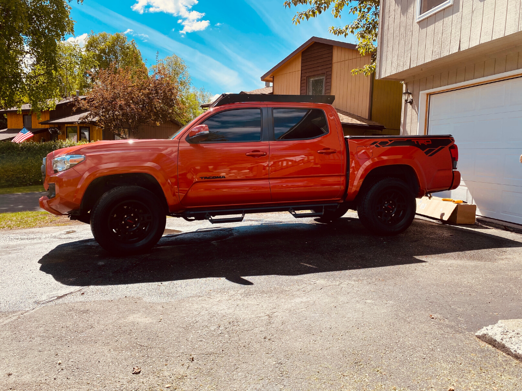 Red Toyota Tacoma TRD parked in residential driveway, featuring black off-road wheels and decals.