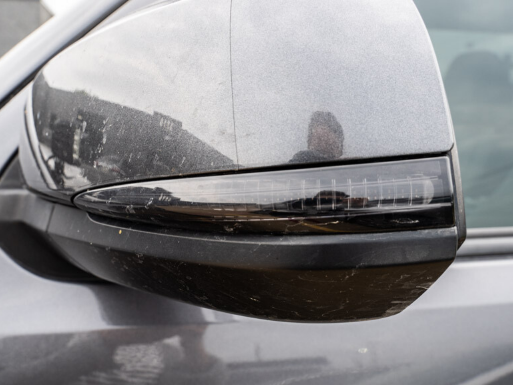 Close-up of a dirty vehicle side mirror with integrated LED turn signal, grey finish