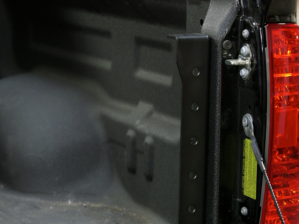 Close-up of a truck bed corner with a metal mounting bracket near the tailgate and taillight