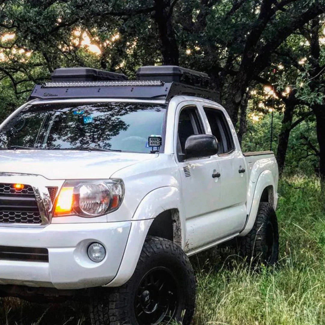 Second generation Toyota Tacoma with ditch light brackets and roof rack parked in a forest