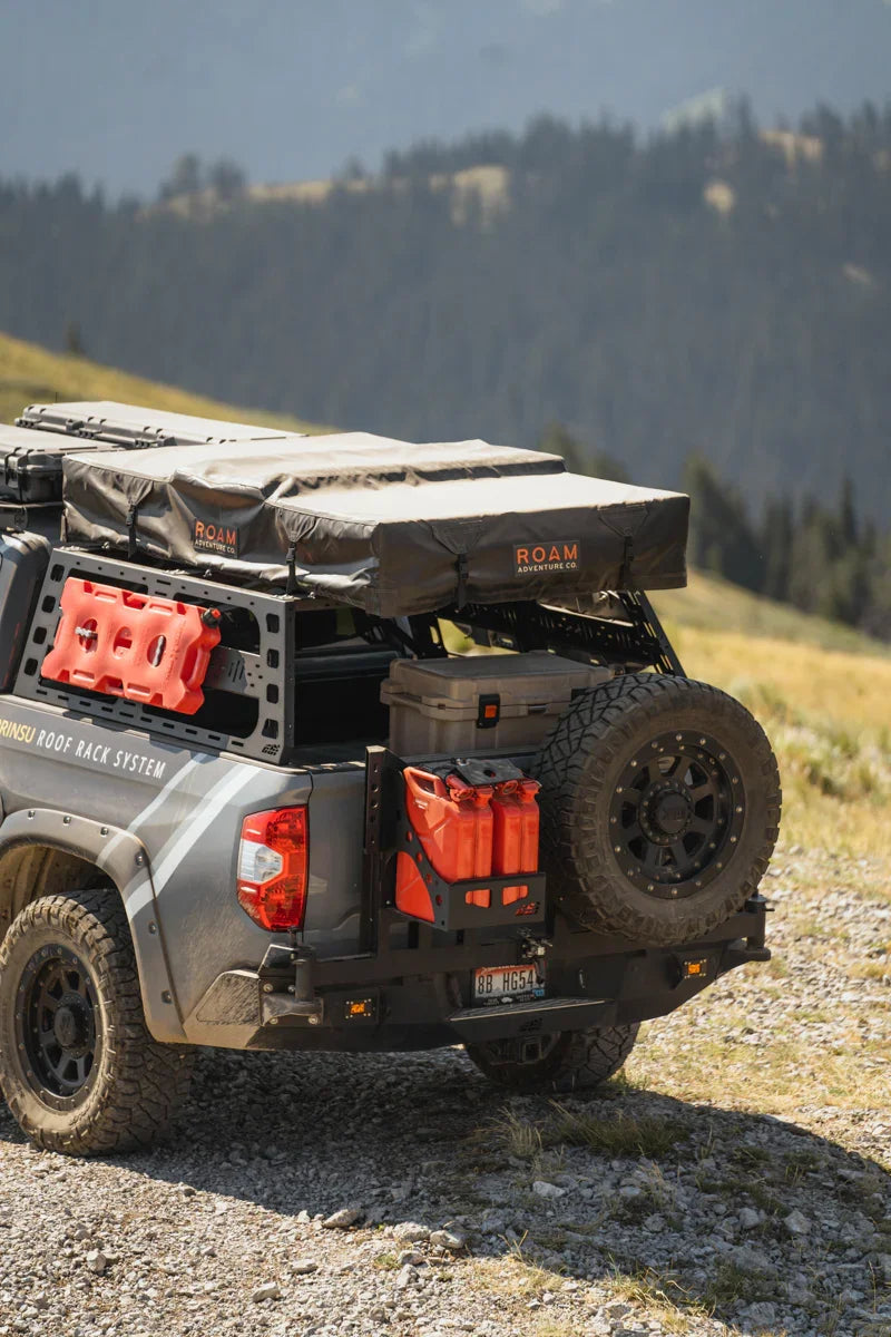 Toyota Tundra with overlanding swing arm, spare tire, fuel cans, and rooftop tent in mountains
