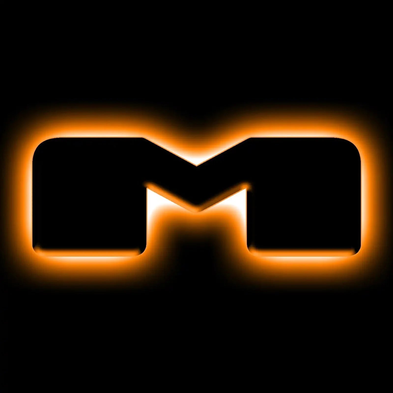 Stylized illuminated M-shaped vehicle badge with orange LED backlight, black background.