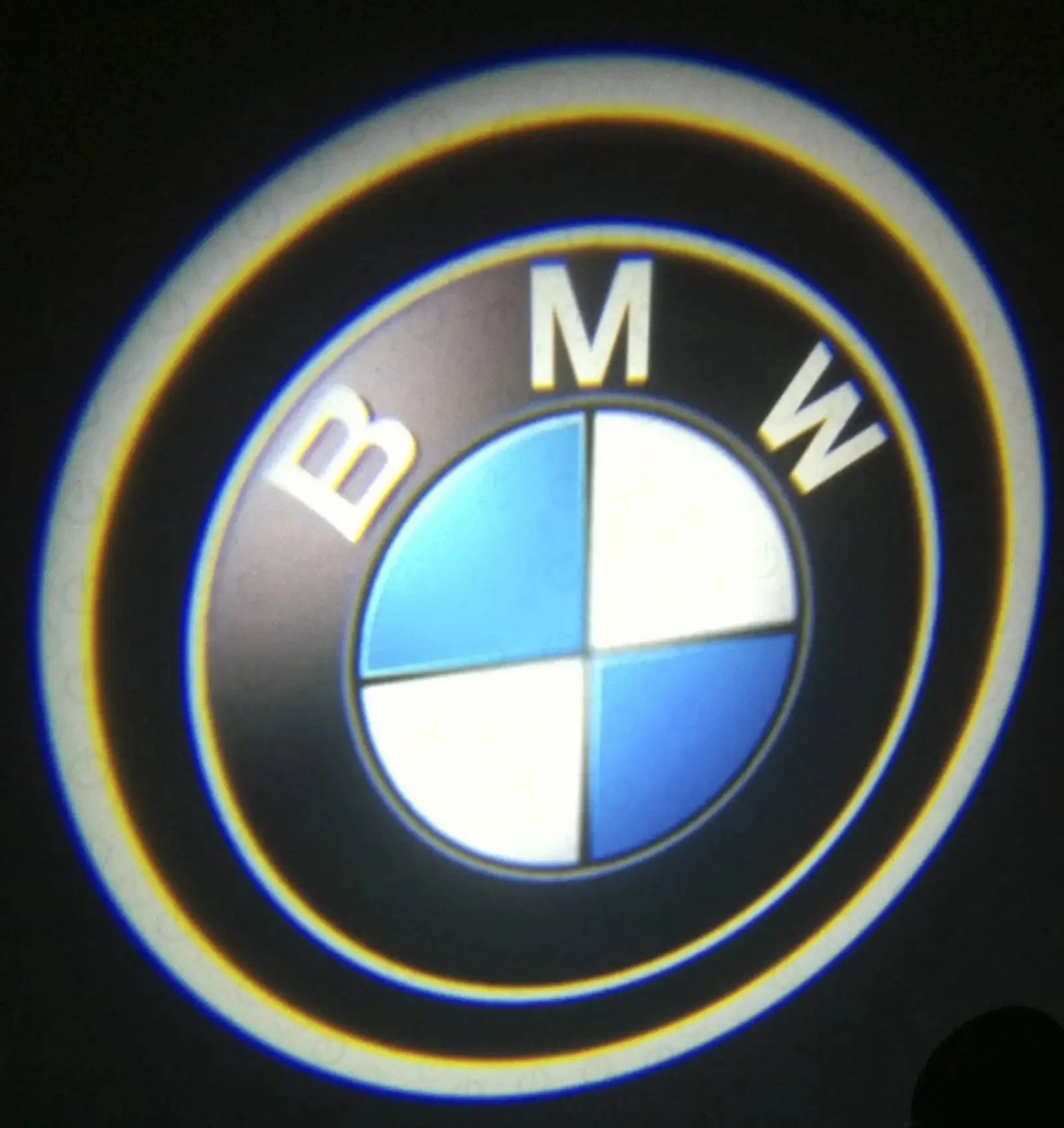 Illuminated BMW car logo projection in blue, white, and black on dark background