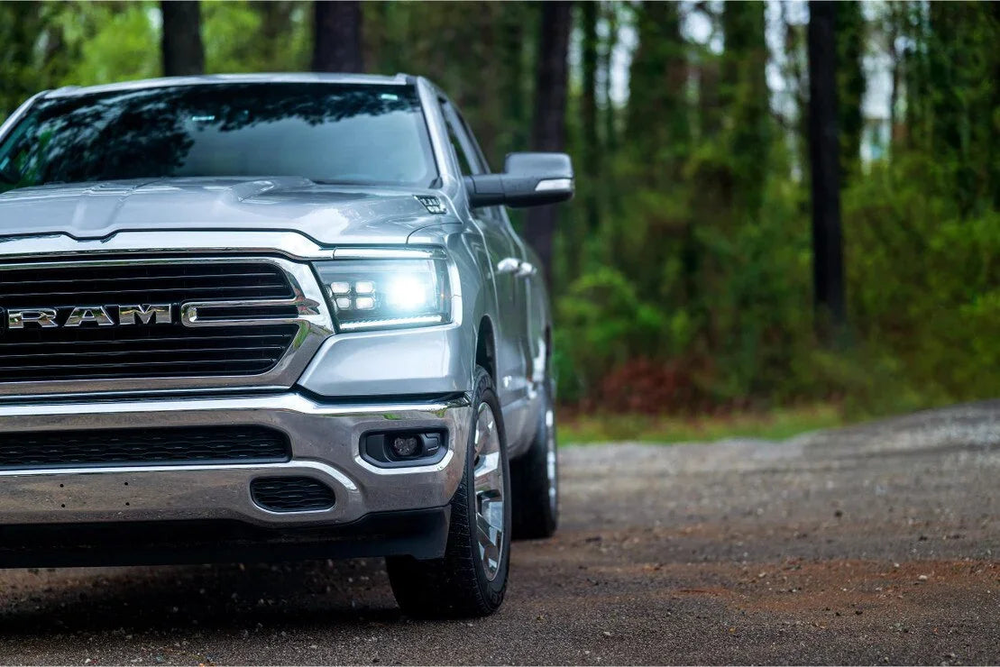 Silver Ram 1500 with bright LED headlights parked on a forest road