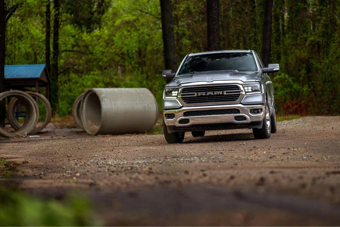 Ram 1500 truck with LED headlights parked outdoors near large concrete pipes and trees