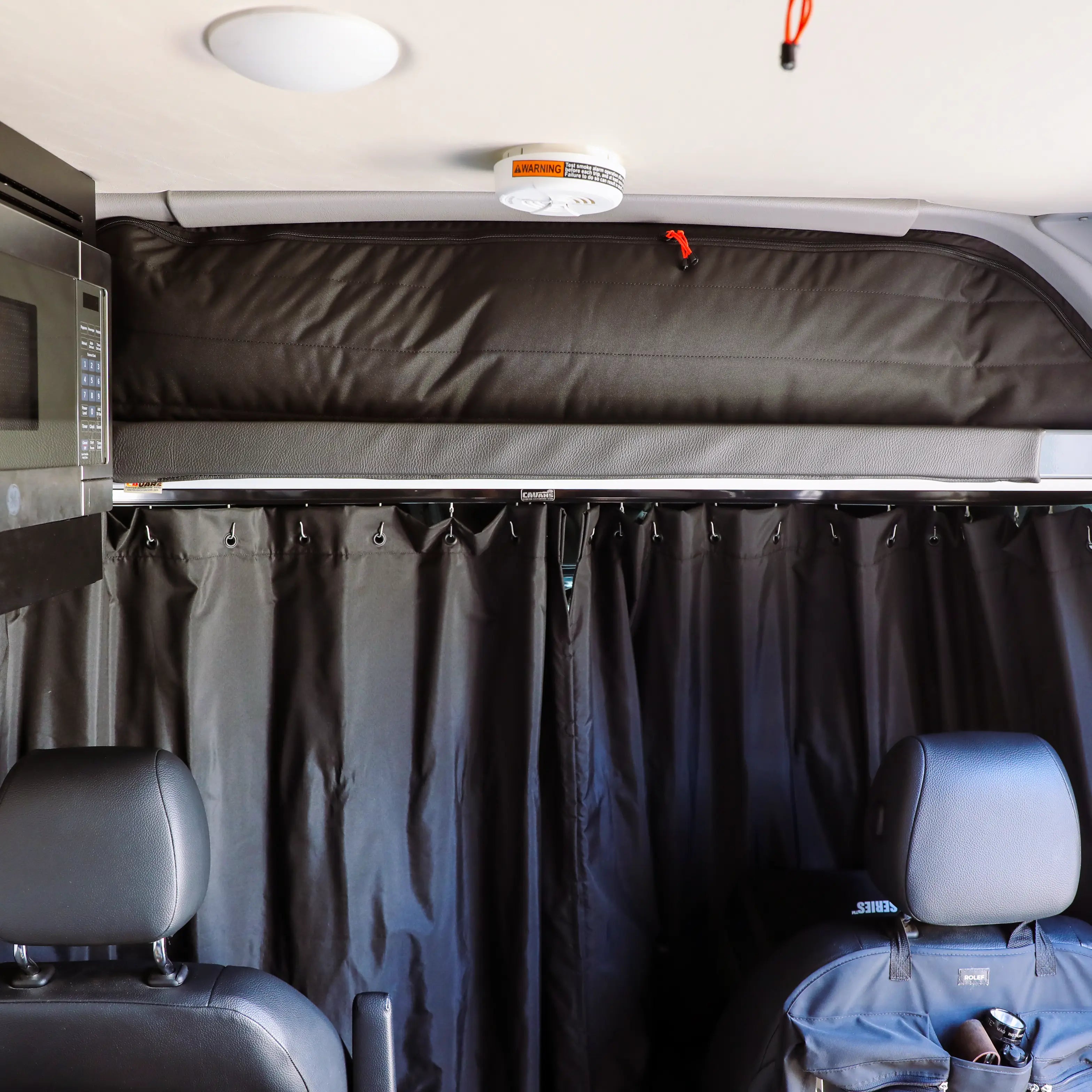 Overland vehicle interior with privacy curtain, driver seats, and overhead storage