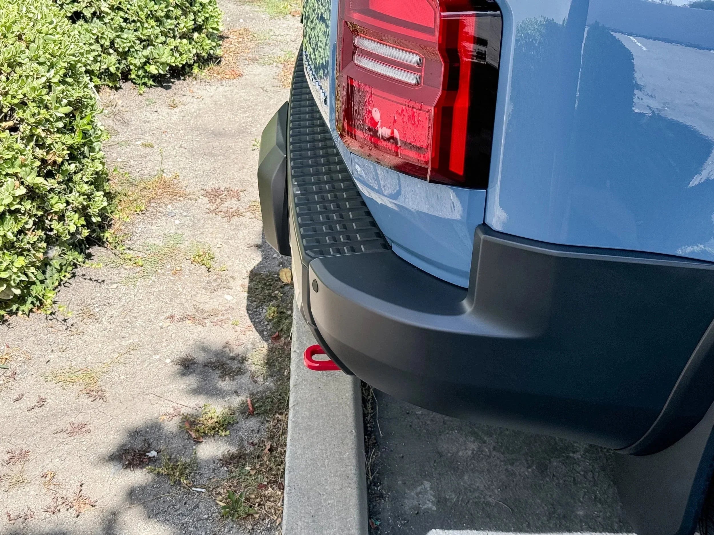 Rear bumper and taillight of a blue overlanding truck parked near curb outdoors