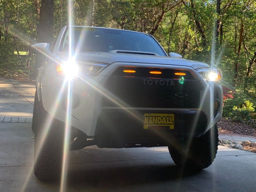 Toyota 4Runner with LED headlights and grill lights parked outdoors in wooded driveway