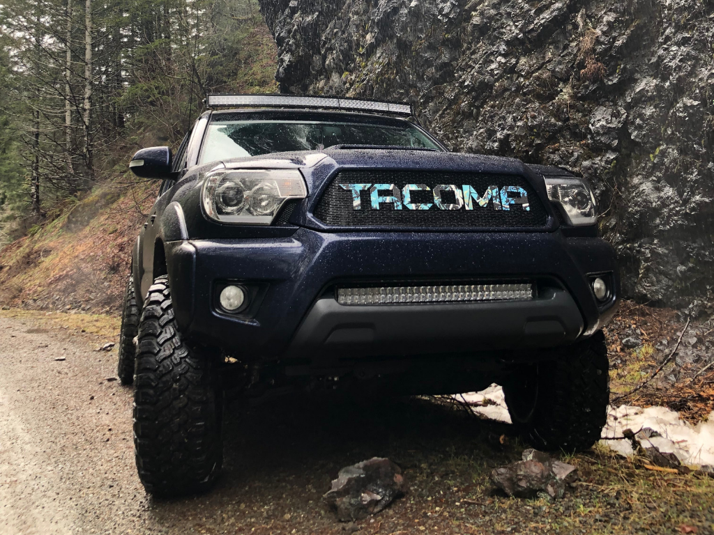 Lifted Toyota Tacoma off-road truck with custom grill and LED light bar on a forest trail