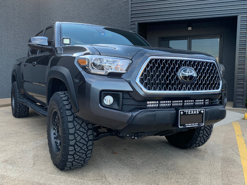 Black Toyota Tacoma truck with off-road tires and LED light bar parked outside modern building