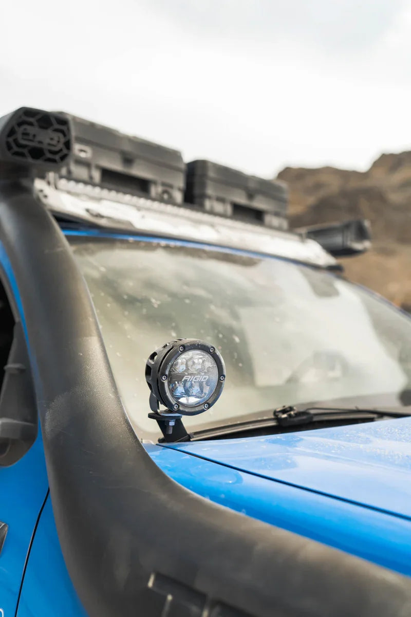 Off-road LED ditch light mounted on blue Toyota Tacoma with snorkel and camping gear