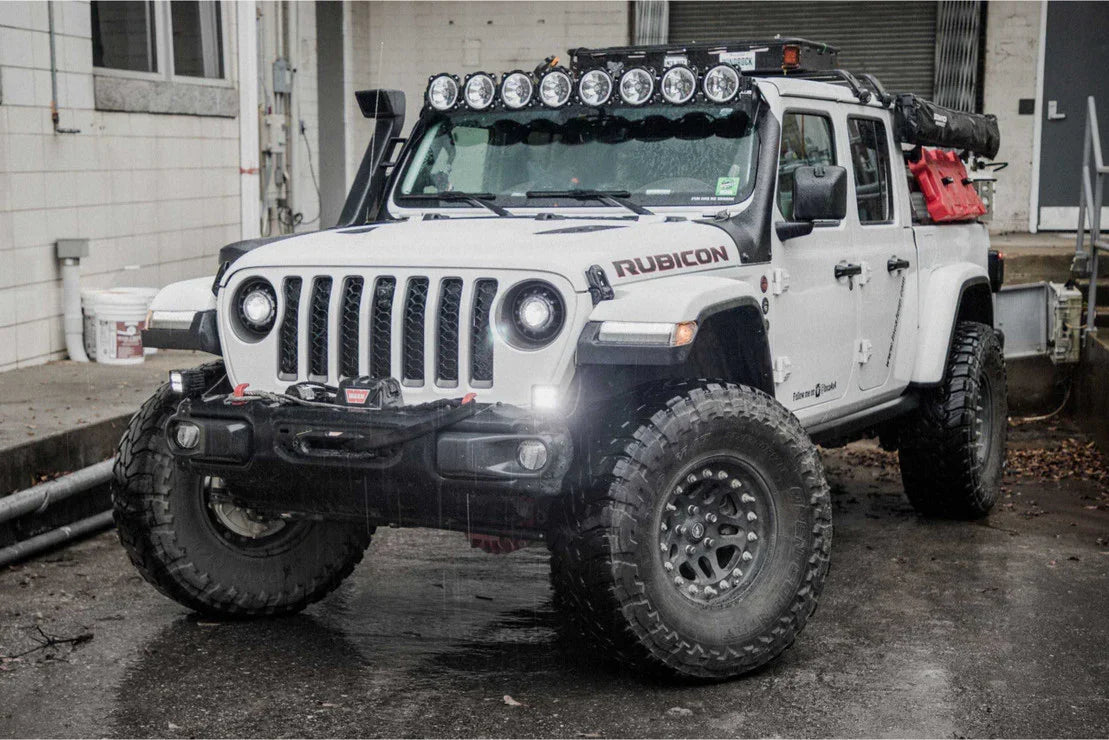 White Jeep Gladiator Rubicon with off-road tires, roof lights, and camping gear loaded