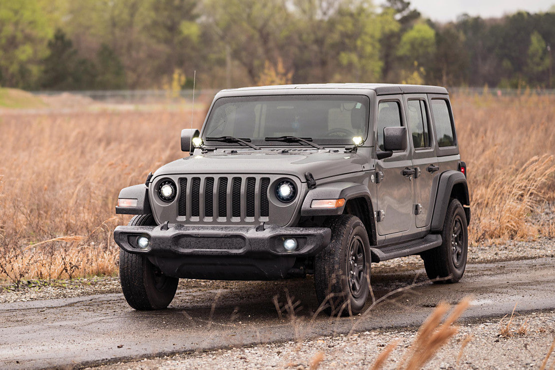 Gray Jeep Wrangler off-road SUV parked on a dirt trail with rugged terrain and bushes.