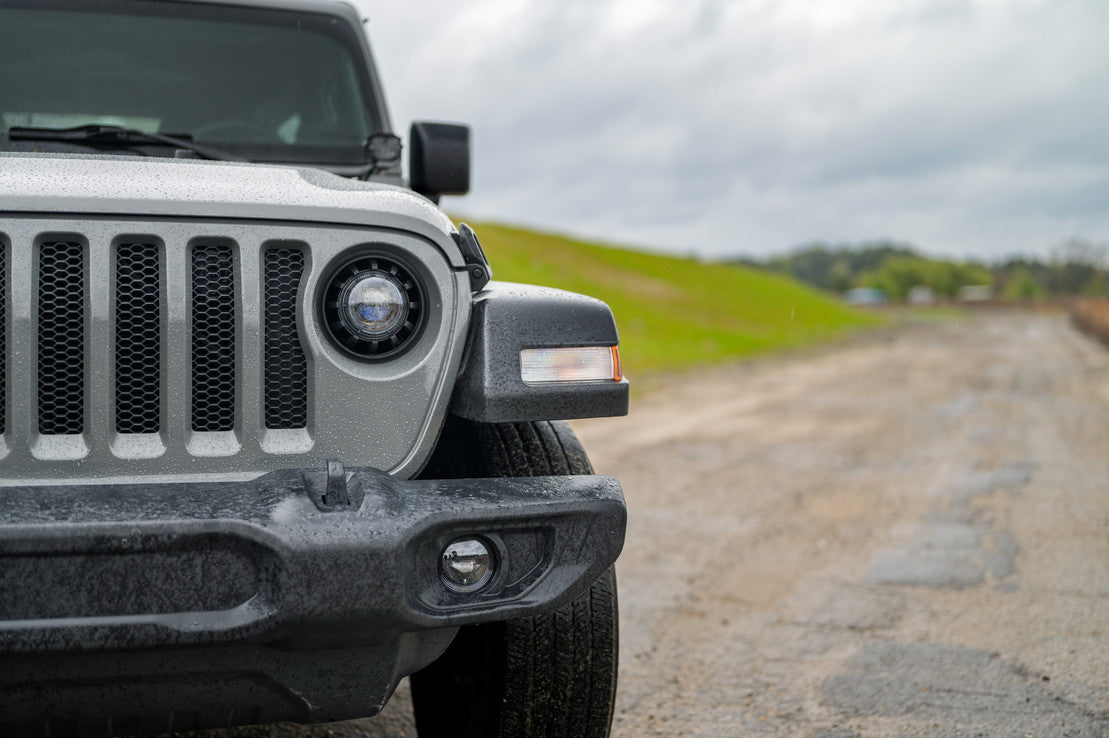 Front view of silver Jeep Wrangler with LED headlight on a gravel road outdoors