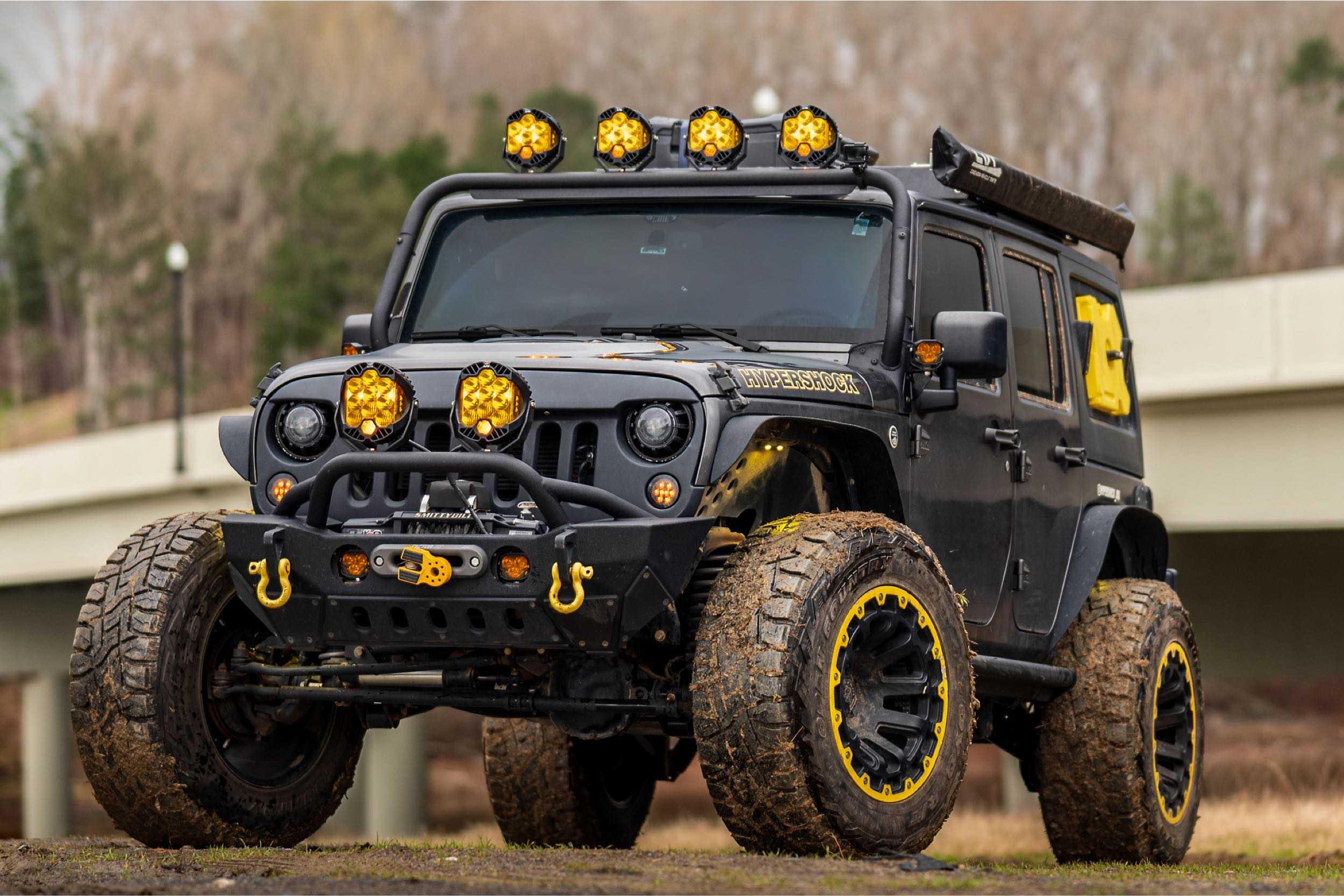 Off-road Jeep Wrangler with yellow accents, mud tires, and roof-mounted LED lights.