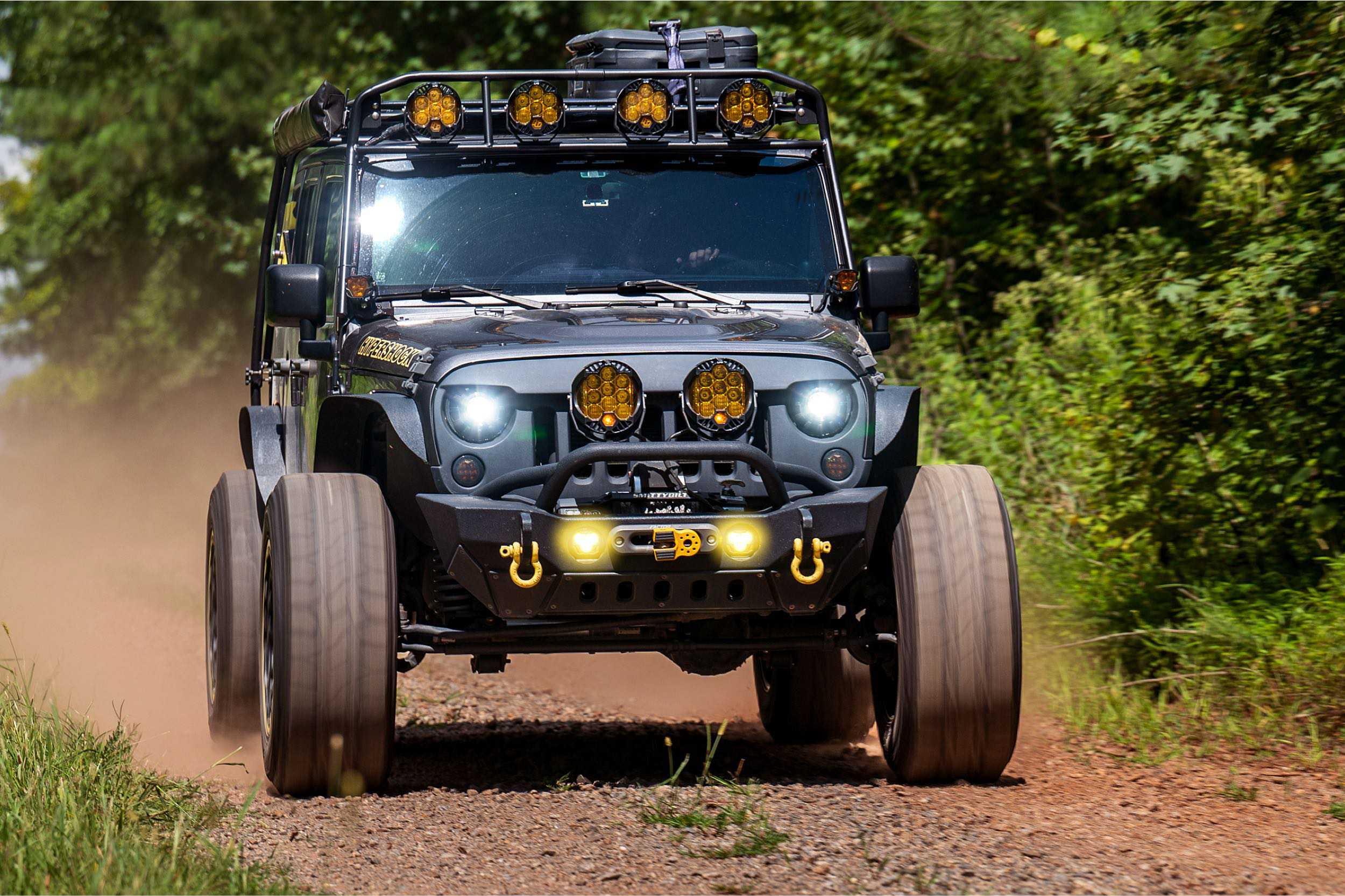 Off-road Jeep with roof rack, extra LED lights, and front bumper on a dirt trail