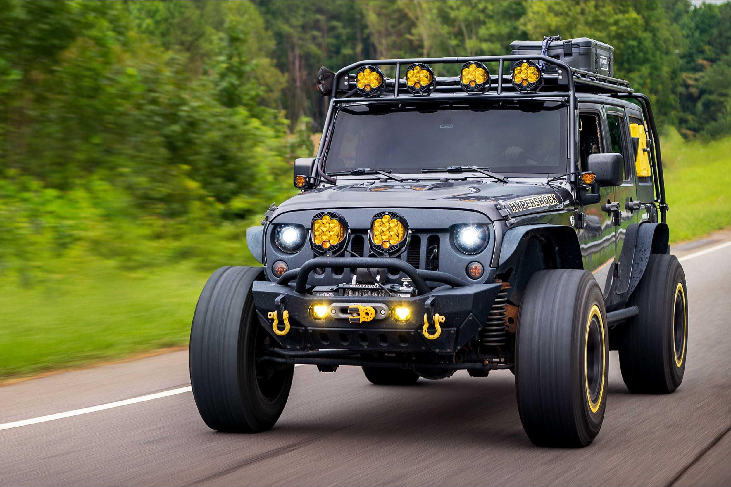 Black Jeep Wrangler with off-road lights and accessories driving on a forest road