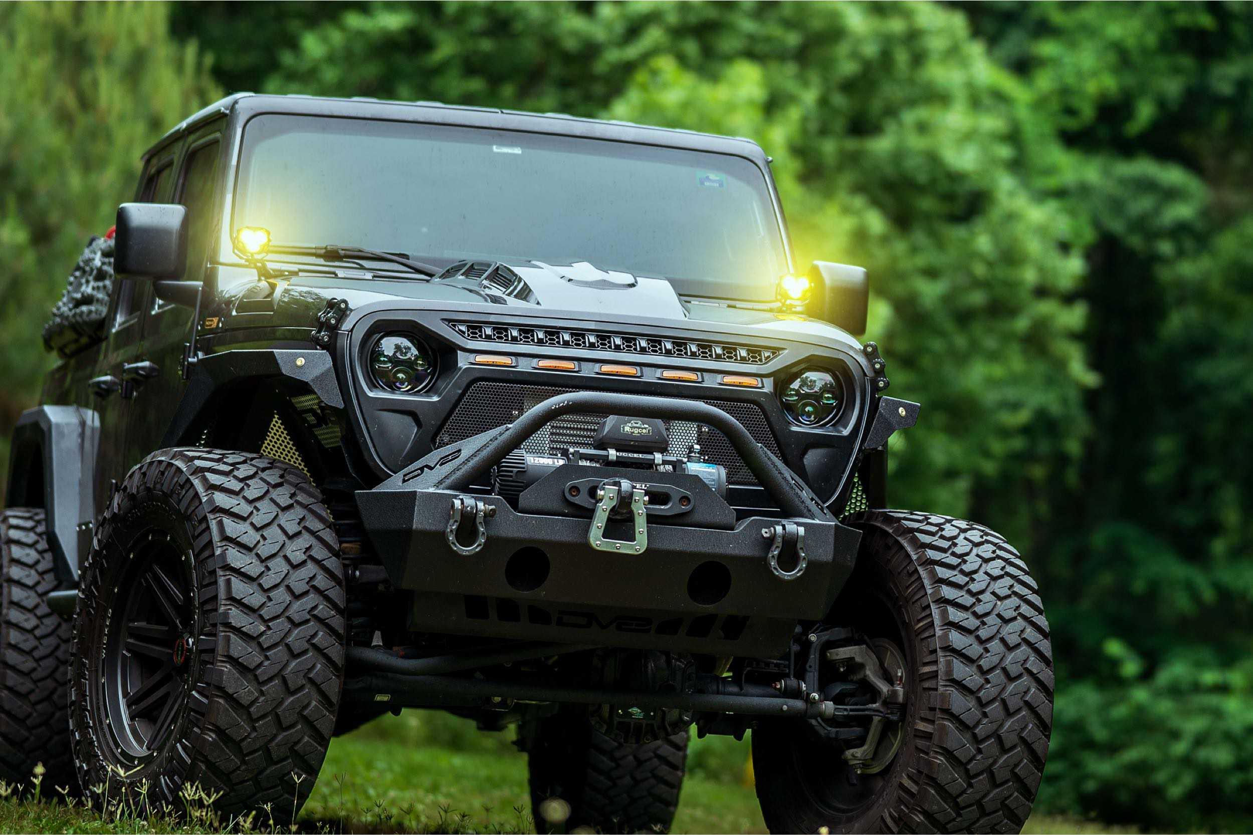 Lifted Jeep Gladiator with off-road tires, aftermarket bumper, and yellow lights in forest