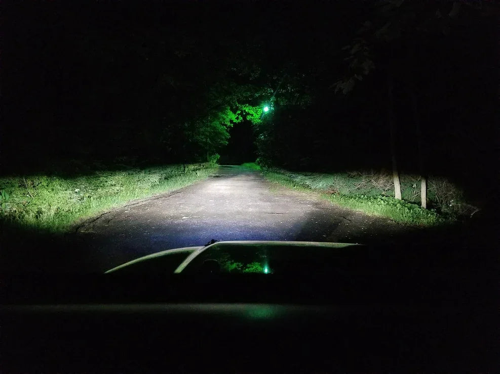Vehicle headlights illuminating a dark forest road at night, ideal for overlanding adventure
