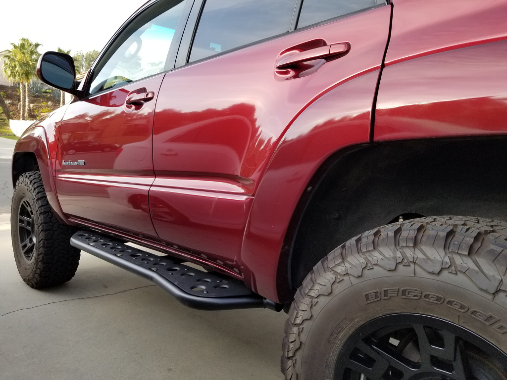 Red Toyota 4Runner with off-road tires and black side step rock sliders for overlanding