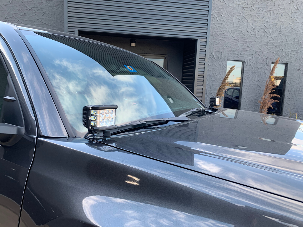 Off-road LED ditch lights mounted on a truck’s hood near windshield, outdoor setting