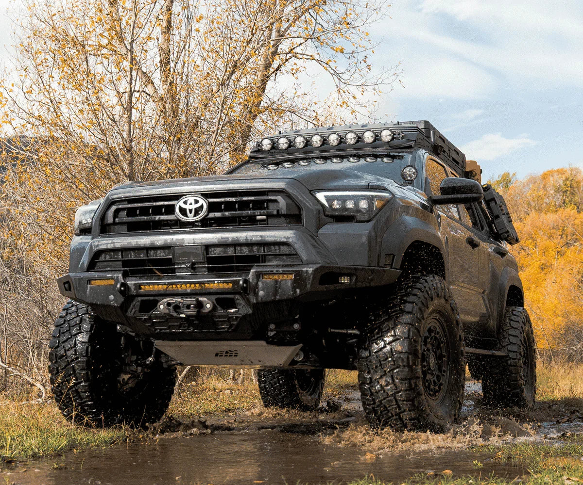 Lifted Toyota 4Runner with off-road tires and expedition gear driving through mud in autumn