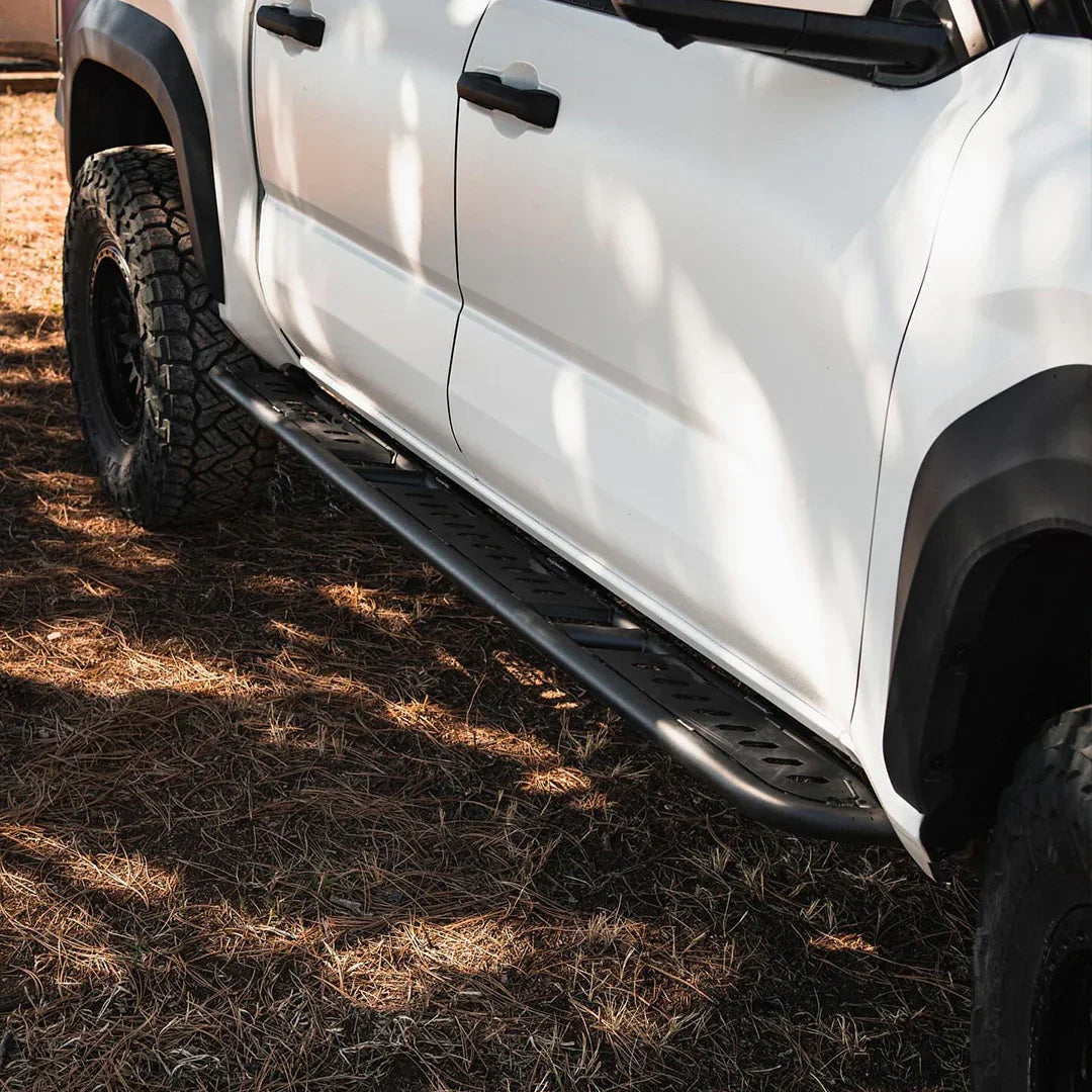 Toyota Tacoma rock sliders on white truck with off-road tires, outdoor ground setting