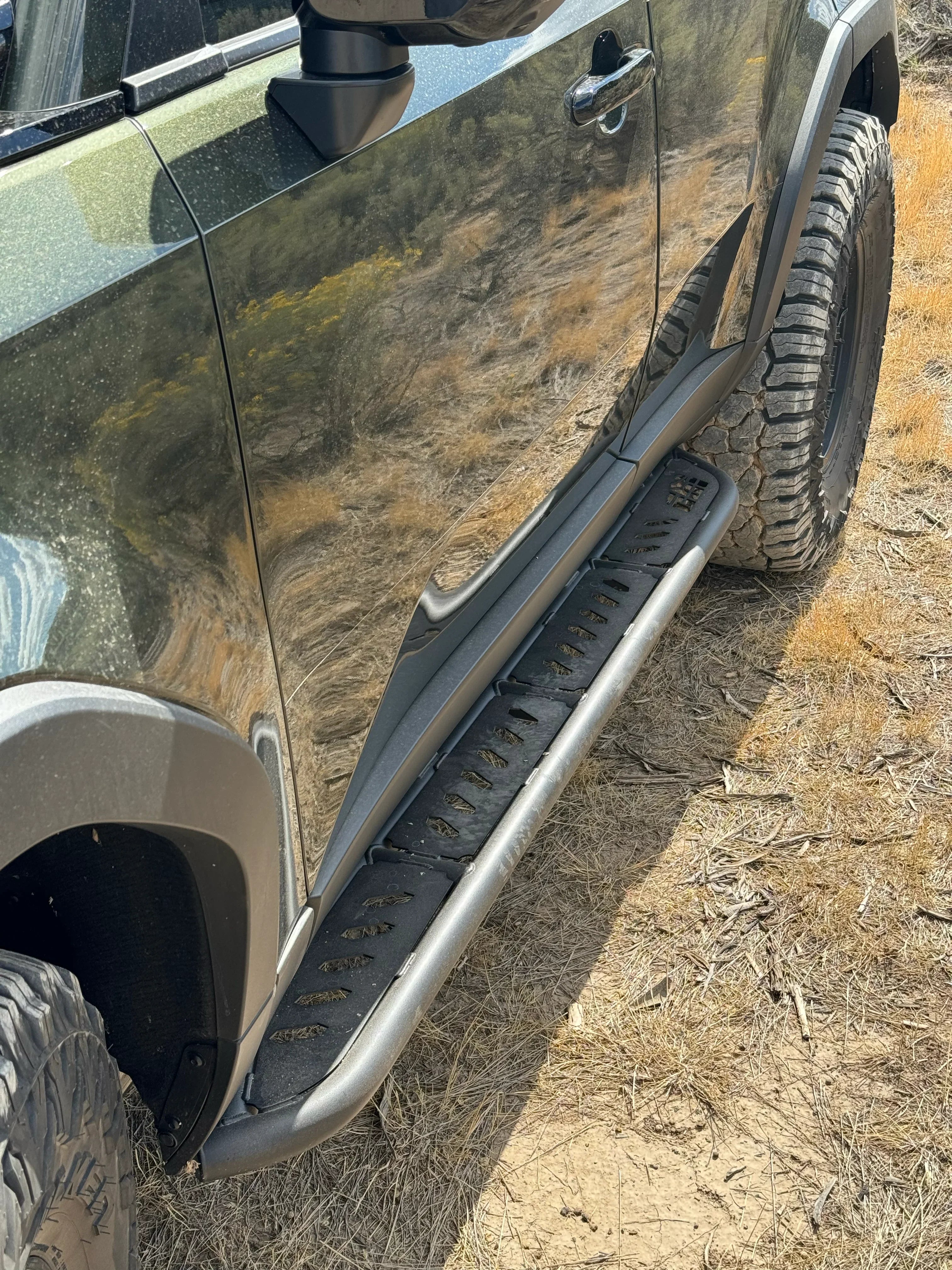 Toyota Tacoma with off-road tires and rugged side step slider on a dirt trail