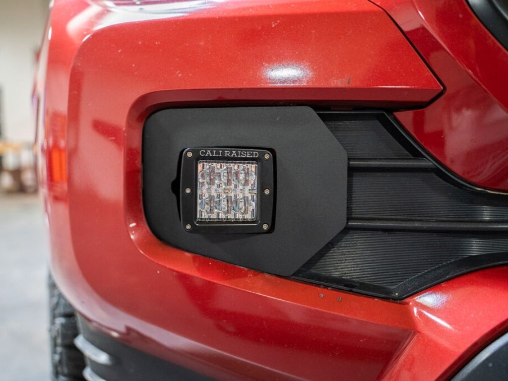 Off-road LED fog light mounted on red Toyota Tacoma front bumper