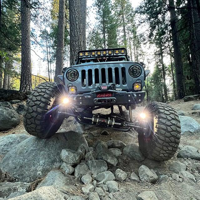 Jeep Wrangler with knuckle lights and off-road tires rock crawling in forest terrain