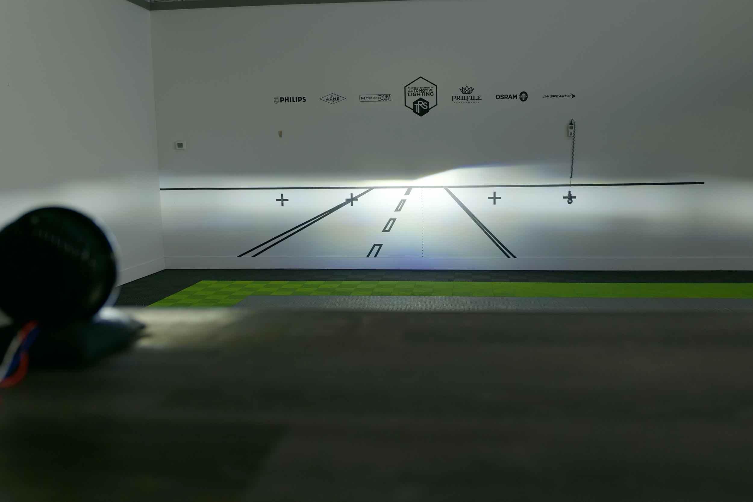 Vehicle headlight beam pattern test against a wall with automotive lighting logos.