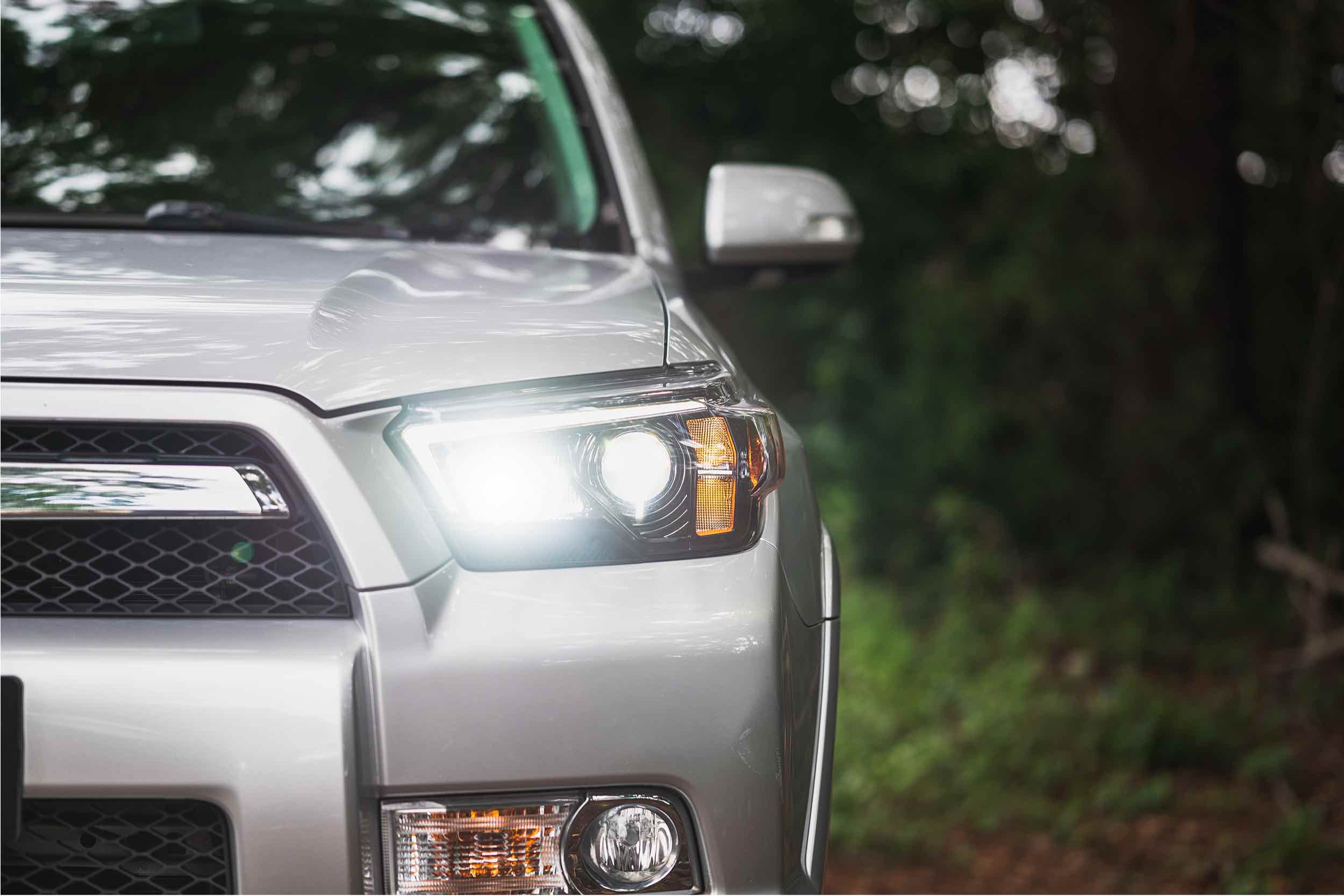 Close-up of silver Toyota 4Runner headlight on with forest background, overlanding vehicle