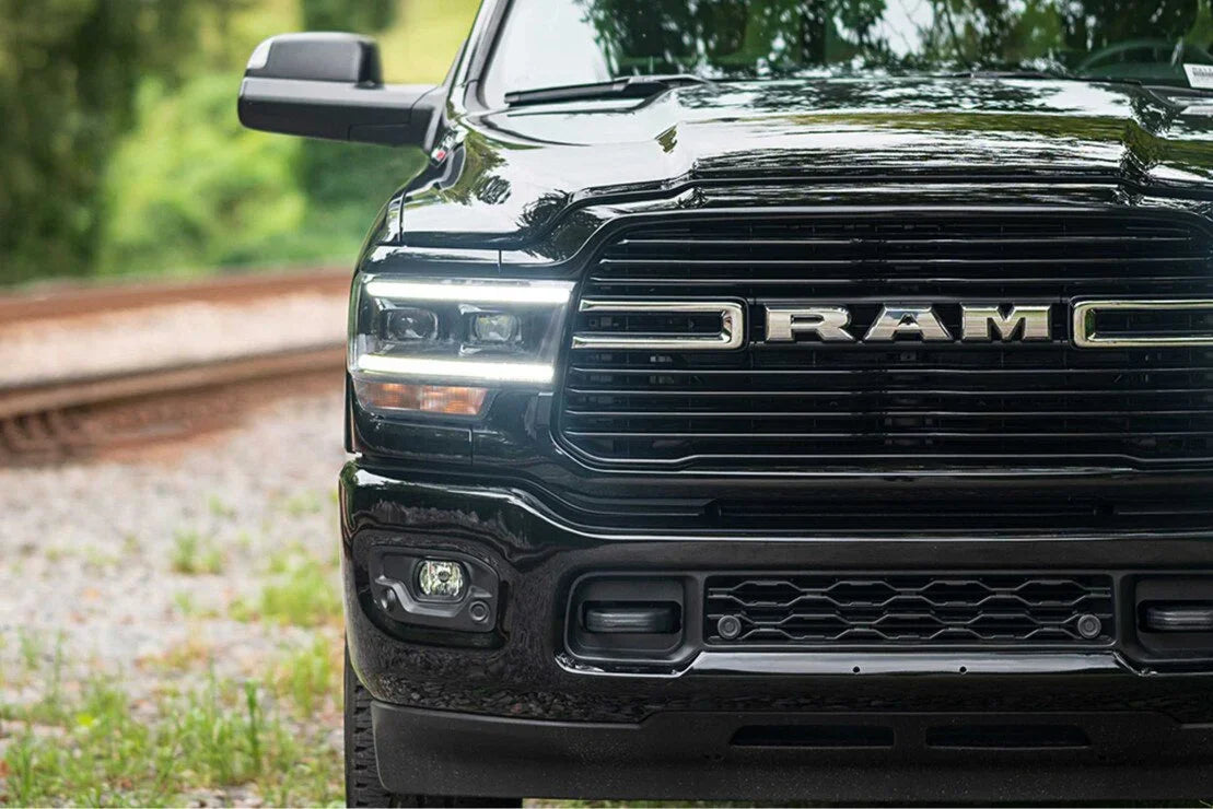 Black RAM truck front grill and LED headlights parked outdoors near railroad tracks