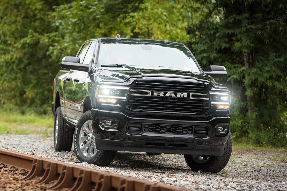Black RAM pickup truck parked on gravel near railroad tracks with wooded background