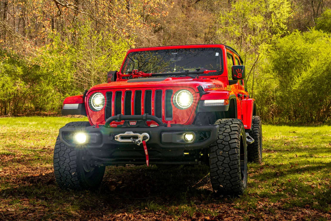 Red Jeep Wrangler with off-road tires, front winch, and lights in a wooded outdoor setting