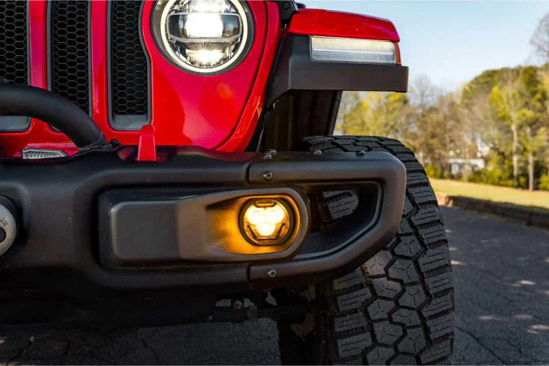 Close-up of red Jeep Wrangler front bumper with illuminated amber fog light and rugged tire.