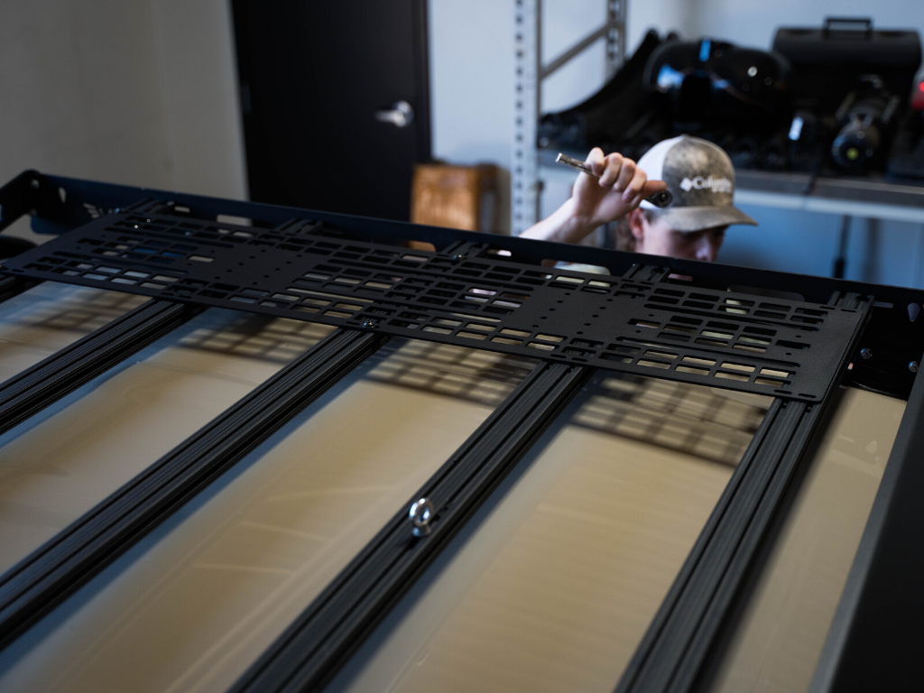 Person installing modular roof rack panel onto overlanding vehicle rack with wrench