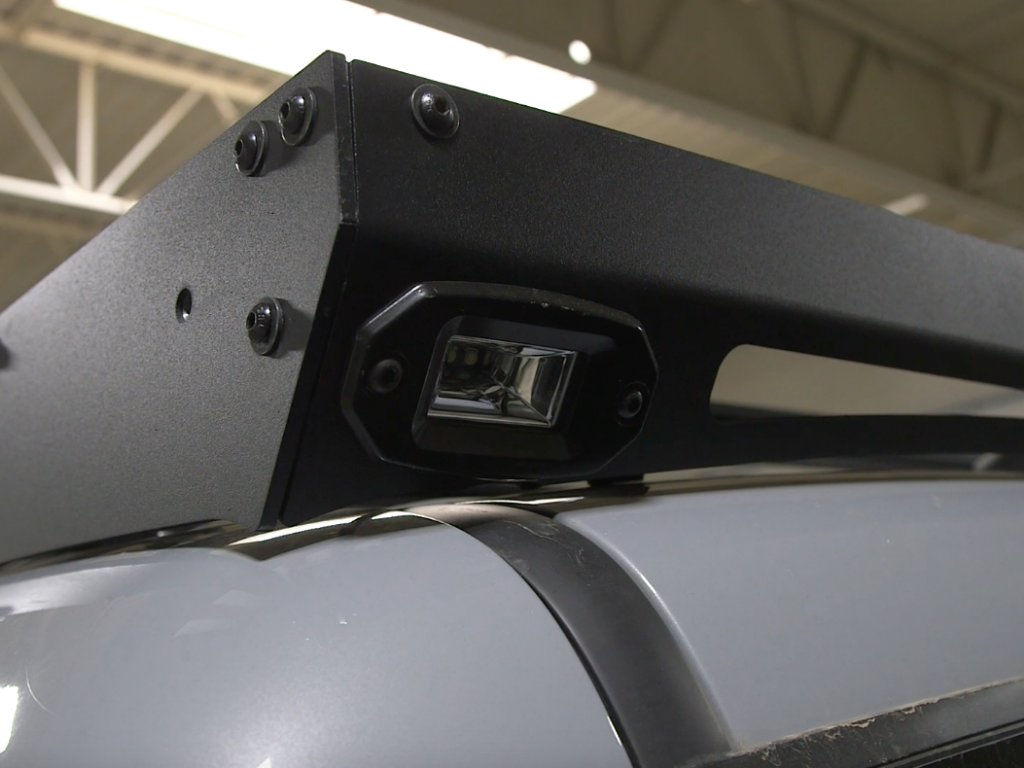 Close-up of a black metal roof rack with integrated LED light on a gray overlanding vehicle