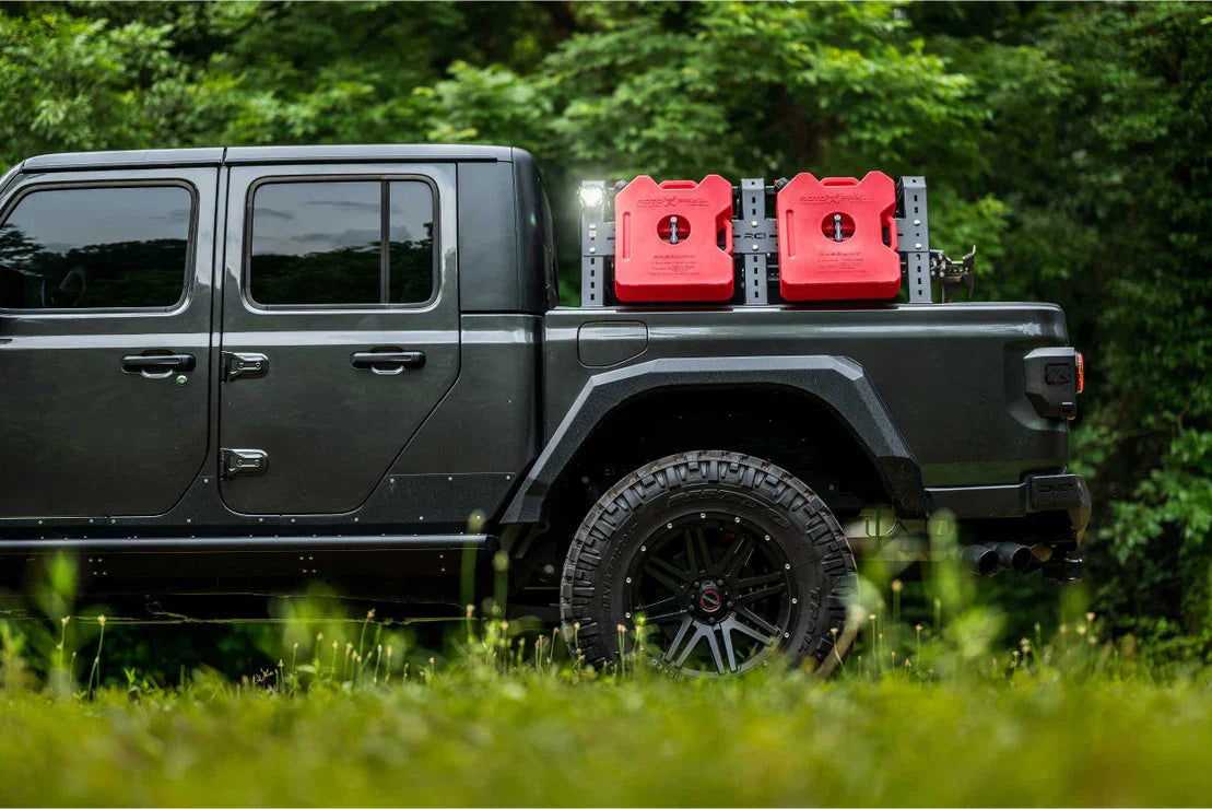 Overland truck with off-road tires and red fuel cans mounted on bed rack in forest setting