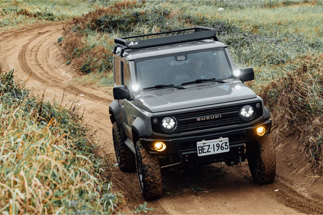 Suzuki off-road vehicle with roof rack driving on a muddy trail in grassy terrain