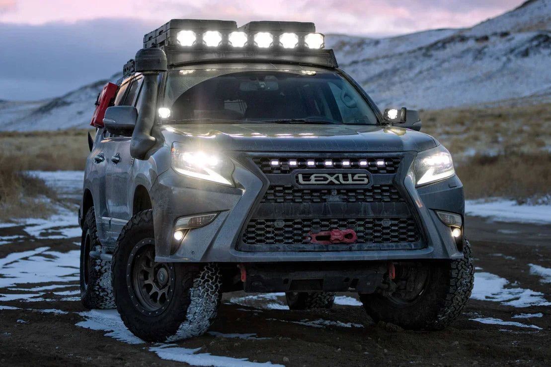 Overland Lexus SUV with off-road tires, roof rack, and LED lights in snowy terrain