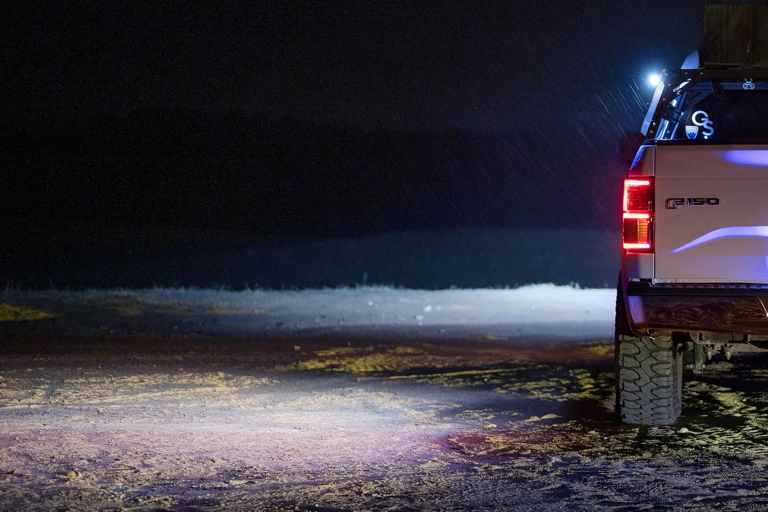 Overlanding truck rear view at night with bright off-road LED lights on dirt terrain