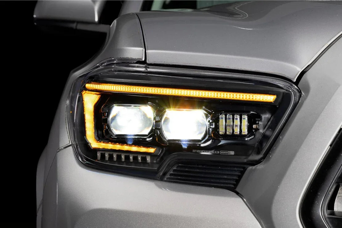 Close-up of LED projector headlights on a gray Toyota Tacoma, amber daytime running lights visible
