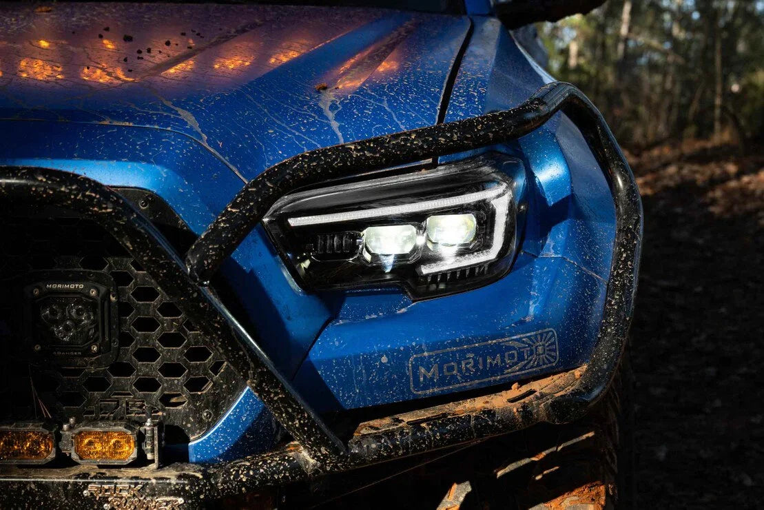 Close-up of aftermarket LED headlights on a blue Toyota Tacoma with off-road mud